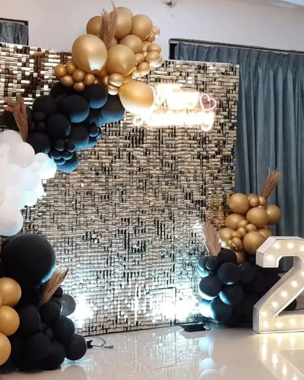 We create stunning backdrops for milestone events, like this 25th-anniversary party. The setup includes a gold shimmer wall, a 'Happy Anniversary' neon sign, and an elegant balloon arch in gold, black, and white.