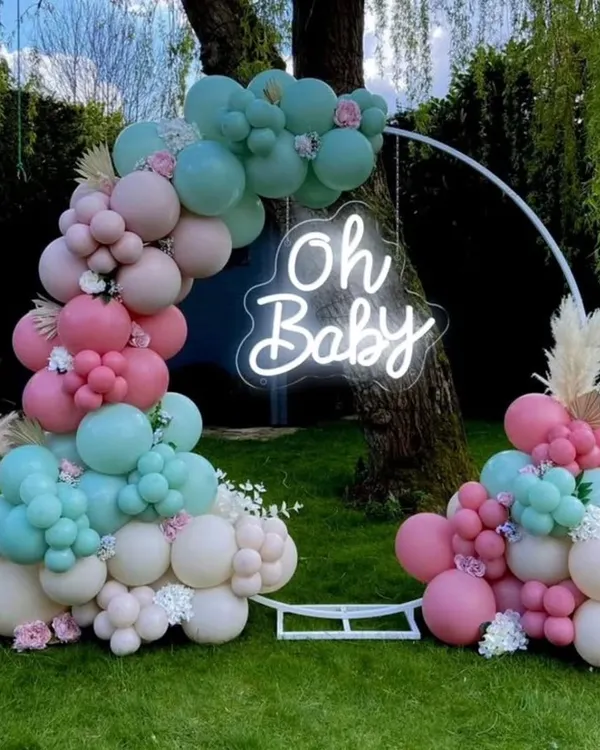 A beautiful outdoor baby shower setup with a circular frame. The decor features a balloon arrangement in pastel pink, teal, and white, and an 'Oh Baby' neon sign, creating a perfect photo opportunity.