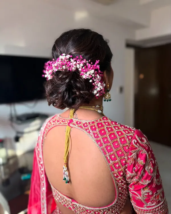 This is one of my signature styles, a soft and textured bridal bun. I've woven in delicate pink and white baby's breath to match the bride's lehenga, creating a romantic look that's perfect for the main wedding ceremony.