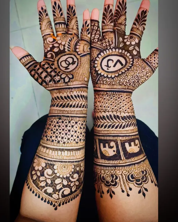 An intricate engagement mehandi featuring the couple's initials "VJ" and interlocking rings, a classic symbol of union. The design is filled with dense, traditional patterns.