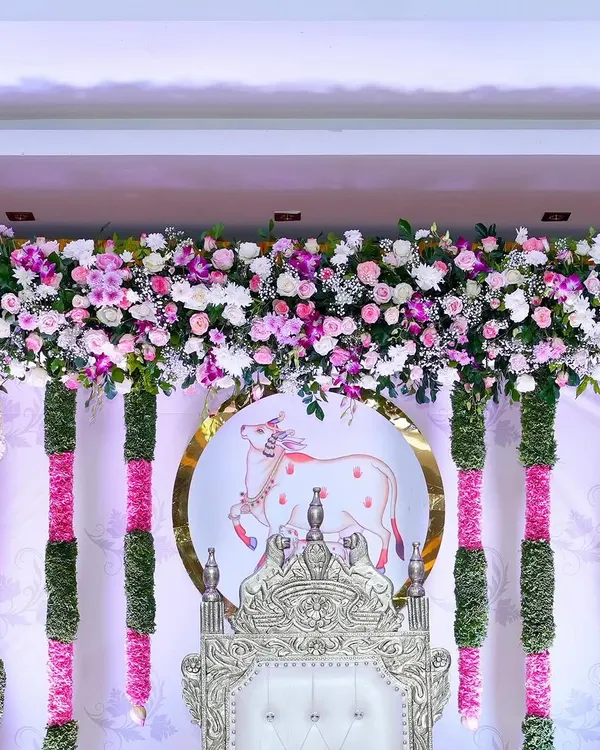 A close-up of the backdrop from a traditional Seemantham. This shows the detail of the fresh flower valance, the hanging garlands, and the custom-printed motif of the holy cow, Kamadhenu, which is significant in these ceremonies.