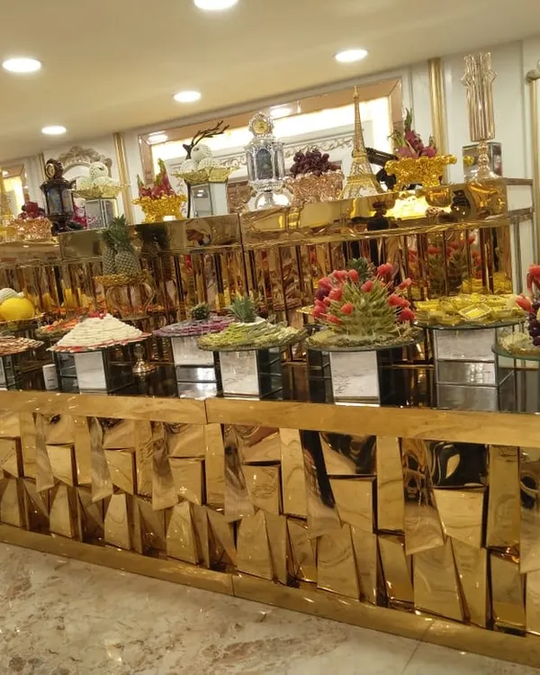 A full view of a luxurious buffet line with a geometric, reflective gold counter. This setup for an indoor event features a wide array of salads, main courses, and fruit displays, showcasing variety and opulence.