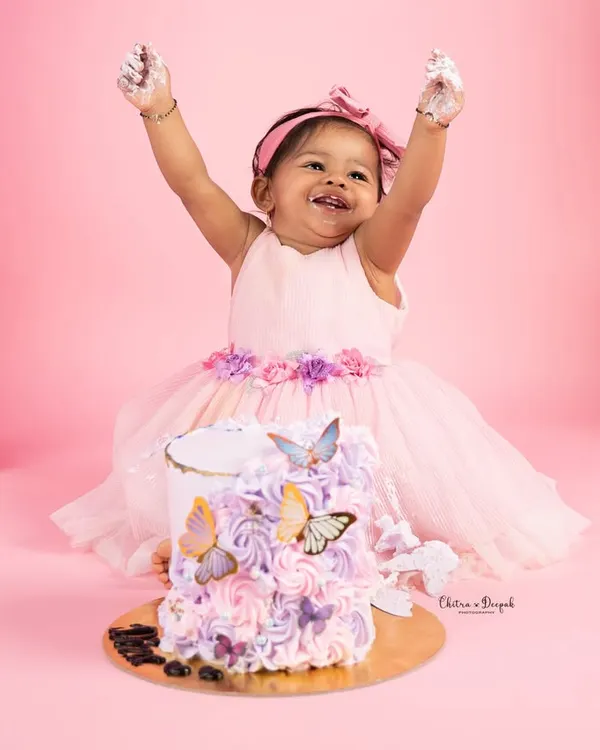 Pure joy and celebration as a little girl, dressed in a lovely pink frock, throws her hands up in delight during her butterfly-themed first birthday cakesmash.