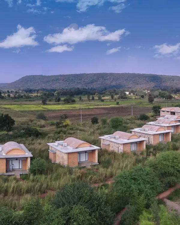 An aerial view of the cottages at Waghoba Ecolodge, nestled in the grasslands near Tadoba. The buildings, with their vaulted roofs made of conical pottery tiles, are designed to merge with the landscape's natural contours and hues.