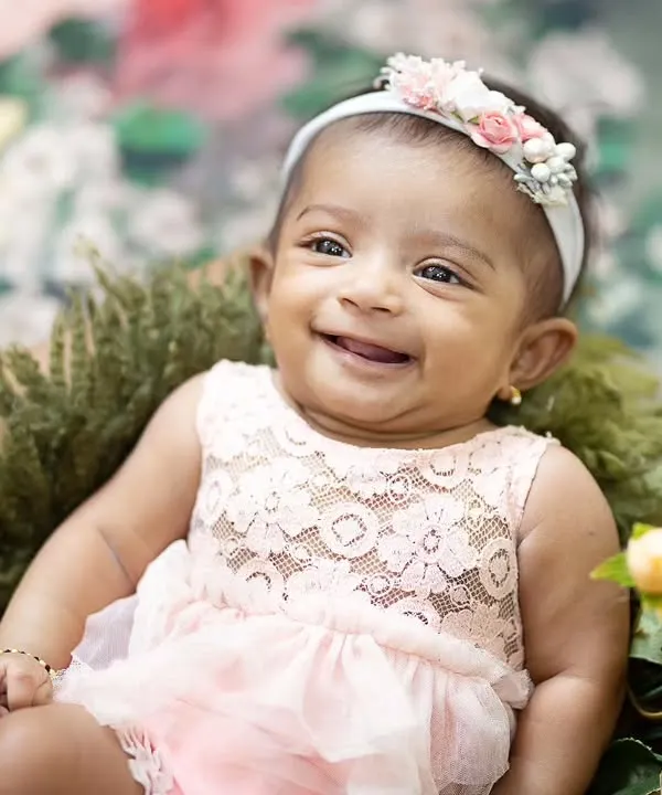 What a heart-melting smile. This baby girl, dressed in a delicate pink lace outfit, is surrounded by yellow flowers for her milestone portrait.