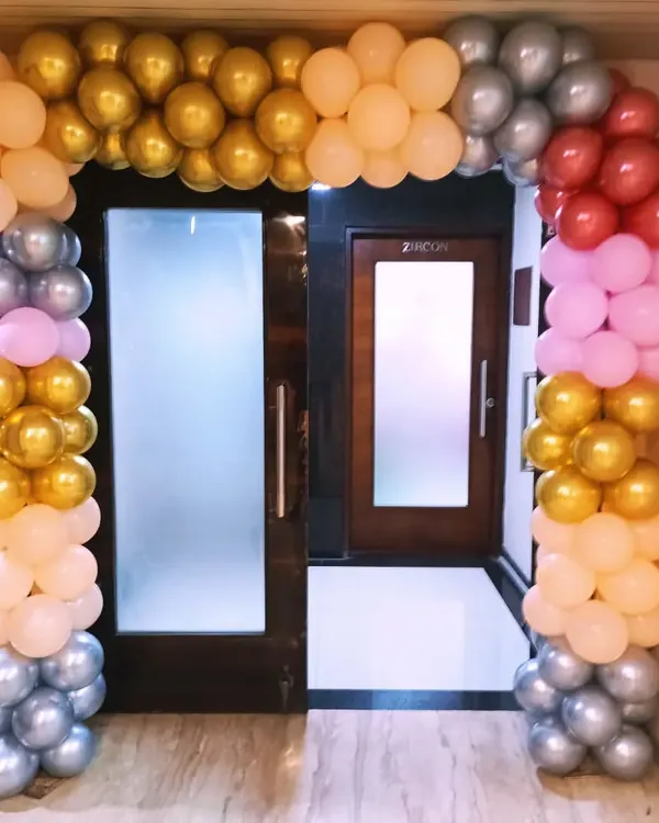 A colorful balloon arch designed to frame an entrance. This arrangement uses a mix of gold, silver, pink, and red balloons to create a welcoming and festive doorway.