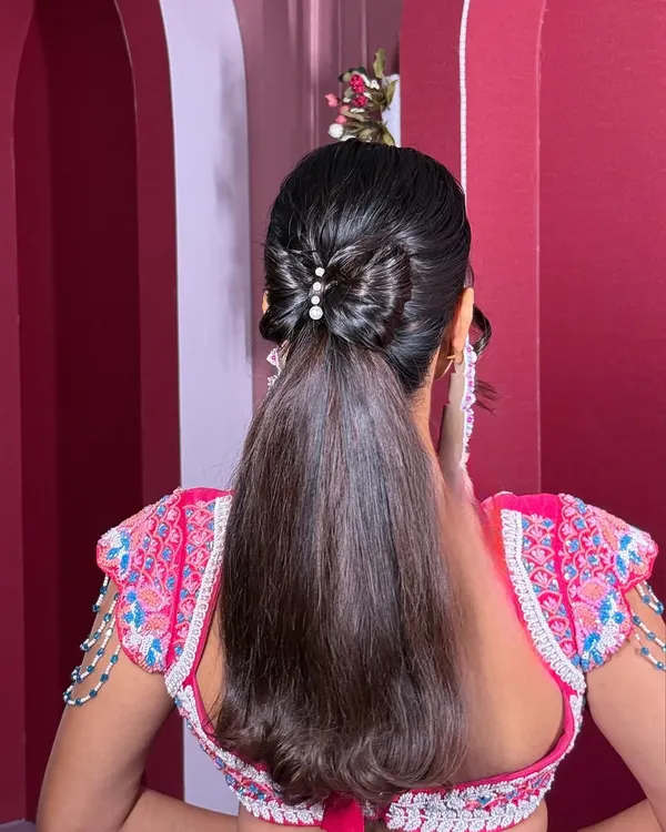 The ultimate "Barbie" ponytail. This style is sleek, high-shine, and features a beautifully crafted bow made from hair, accented with pearls for a touch of elegance.