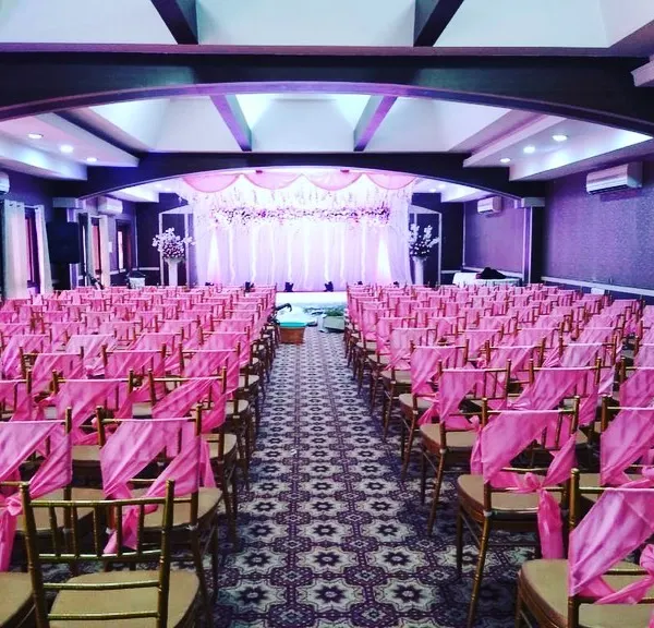 A large hall prepared for a corporate awards ceremony or gala dinner. The chairs are elegantly decorated with pink sashes, and the stage is set for presentations and entertainment, creating a celebratory atmosphere.