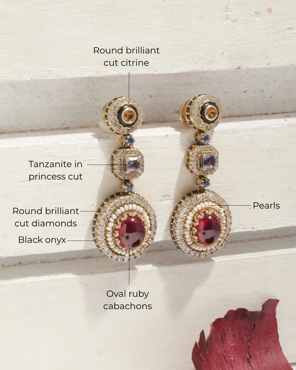A detailed view of the iconic Crimson Royal earrings. This piece is a treasure trove of gems, featuring oval ruby cabochons, princess cut tanzanite, round brilliant citrine, pearls, and black onyx accents.