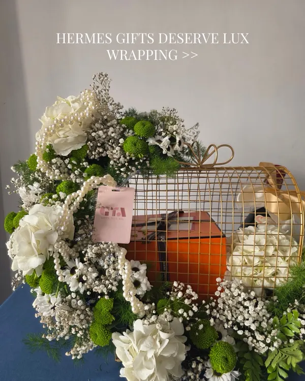 A luxury gift deserves a grand entrance. Here, I've placed a signature orange Hermès box inside a golden cage, surrounded by an explosion of white and green florals to create an unforgettable unboxing experience.
