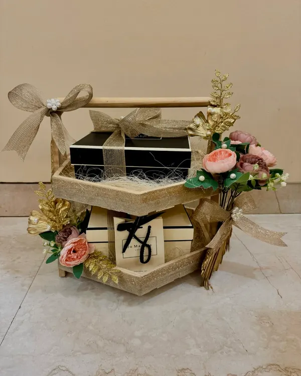 A beautiful two-tiered wooden stand used for wedding gift presentation, adorned with Jo Malone boxes and delicate floral arrangements. This is part of my 'Shaadi ke Tohfe' service.