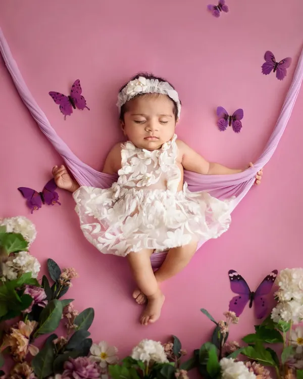 Like a little fairy sleeping in a garden. This setup features a soft fabric hammock, surrounded by flowers and butterflies, creating a beautiful and whimsical portrait for a baby girl.