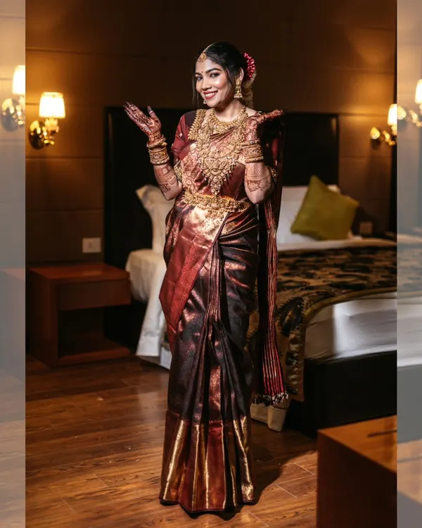 A joyful bridal portrait, capturing the bride's excitement and her stunning, shimmering saree in a warmly lit room.