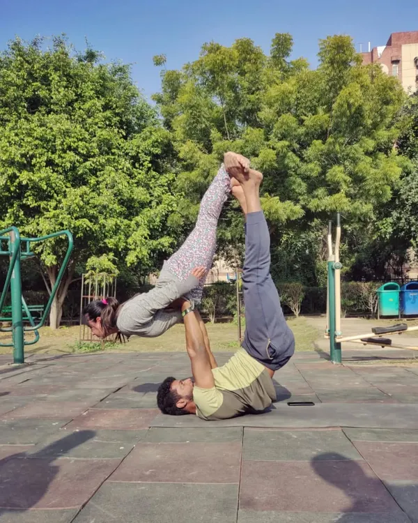 A classic Acro Yoga pose called "Bird" being performed in a park. This partner exercise is fantastic for building core strength for the base and balance for the flyer.