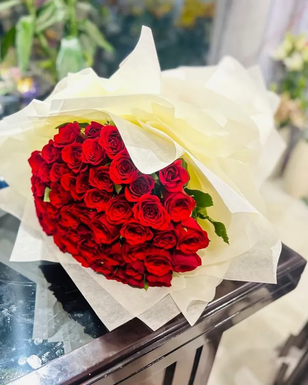 A large, classic bouquet of fresh red roses, wrapped in simple cream paper to let the flowers stand out. This is a timeless gift for expressing love and appreciation.