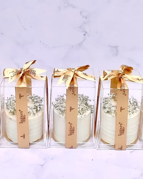 A row of my elegant mini cakes, each individually packaged in a clear box with a gold ribbon. Topped with delicate baby's breath, these are perfect as sophisticated wedding or party favors.