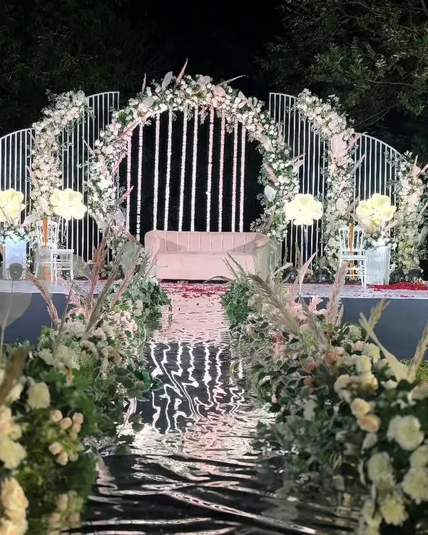 This is where your forever begins. We designed this breathtaking reception stage with a reflective mirror aisle, flanked by lush white florals and pampas grass, creating an ethereal pathway for the couple's grand entrance under the stars.