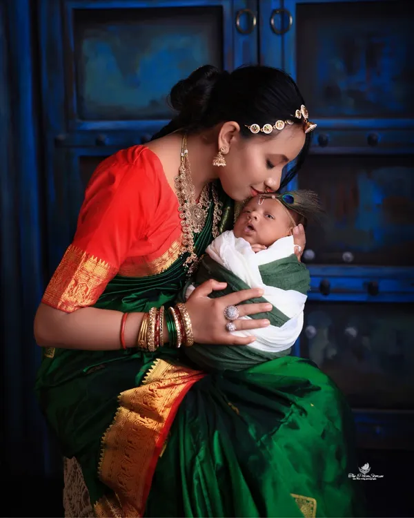 A timeless portrait capturing the tender bond between a mother and her newborn. Dressed in a beautiful traditional saree, she holds her baby close, creating a classic and emotional image against a deep blue, artistic backdrop.