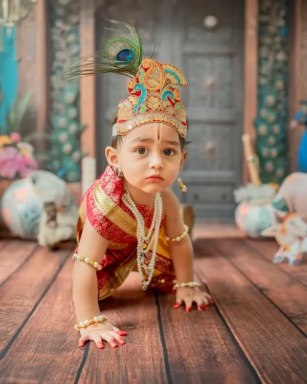 A crawling 'Little Krishna' on a mission. This dynamic shot captures a key baby milestone within the vibrant Janmashtami theme, complete with a peacock feather crown and traditional jewelry.