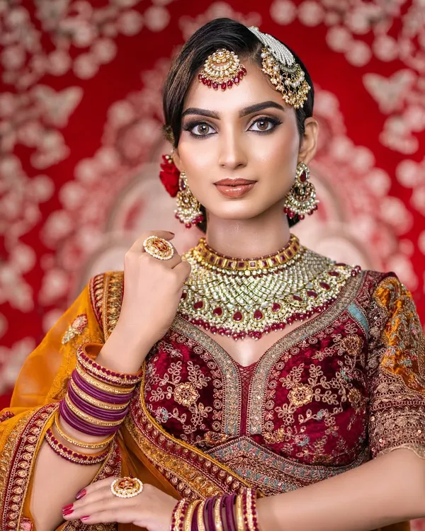 A regal North Indian bridal portrait. This image captures the intricate details of the makeup, from the sharp cut-crease eye to the perfectly blended base, complementing the rich colors of the lehenga.