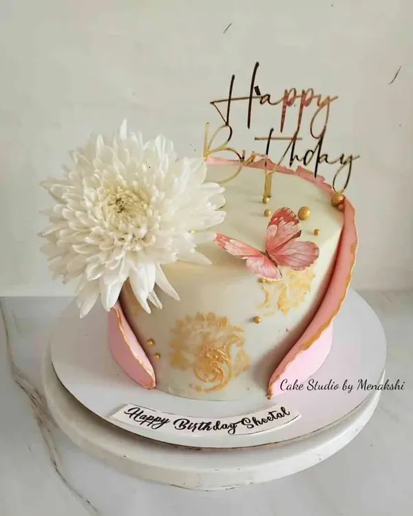 A pretty birthday cake featuring a large fresh chrysanthemum, a hand-painted butterfly, and a delicate fondant wrap. The gold stenciling adds a touch of elegance to the design.