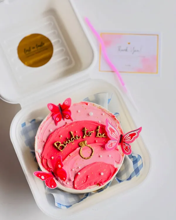 A beautiful "Bride to be" bento cake perfect for a bridal shower or bachelorette party. It features an ombre pink design, a gold ring detail, and decorative butterflies.
