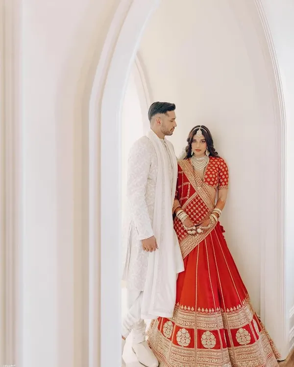 The stunning couple, Carla and Arjun, in a quiet moment. Carla's classic red Sabyasachi lehenga is beautifully contrasted by Arjun's elegant all-white sherwani, creating a timeless and romantic visual.