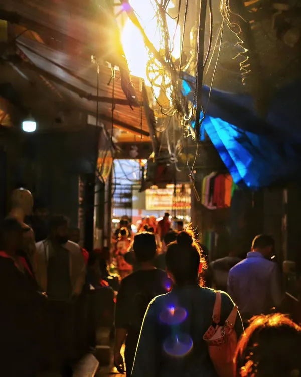The sensory experience of a crowded street is captured in this photo. The bright overhead light, tangled wires, and the movement of the crowd create a scene so immersive you can almost smell the street.