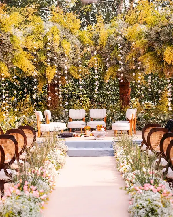 A breathtaking outdoor mandap setup for a day wedding, with lush greenery and hanging floral arrangements creating a fairytale atmosphere.