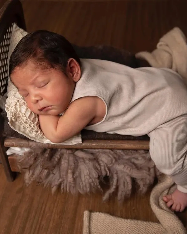 A newborn peacefully sleeping in a miniature wooden bed. I use props like these to highlight just how tiny and precious they are in their first days.