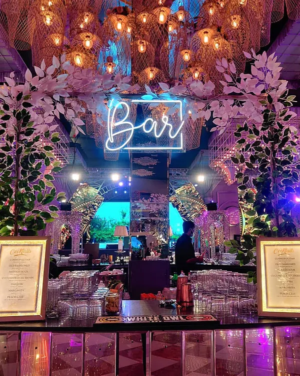 A beautiful bar setup for a reception at Ritz by FNP. The white floral arches, mirrored bar front, and neon sign create an elegant and modern focal point for the event.