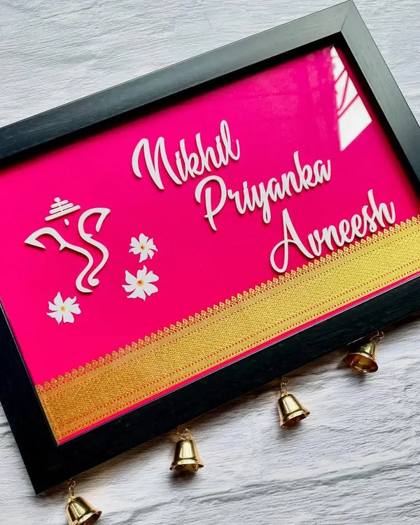 A beautiful Khun nameplate in a vibrant pink, customized in English with a Ganesha icon for blessings. The little bells at the bottom add a lovely traditional sound and look.