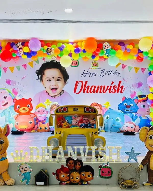 A bright and cheerful Cocomelon party stage, featuring a large personalized backdrop with the birthday boy's photo and all the main characters.
