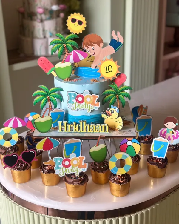 Pool party, but make it cake. This fun and vibrant pool party themed cake is surrounded by matching cupcakes, complete with tiny umbrellas, beach balls, and sunglasses. It's the perfect centerpiece for a summer birthday.