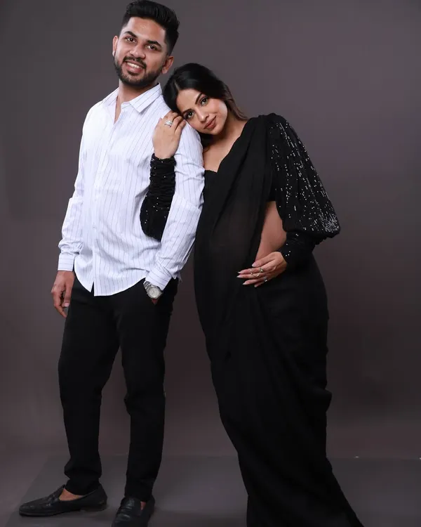 A modern take on a traditional look. The mom-to-be wears a stylish black saree with sequined sleeves, resting her head on her partner's shoulder for a sweet and contemporary couple's portrait.