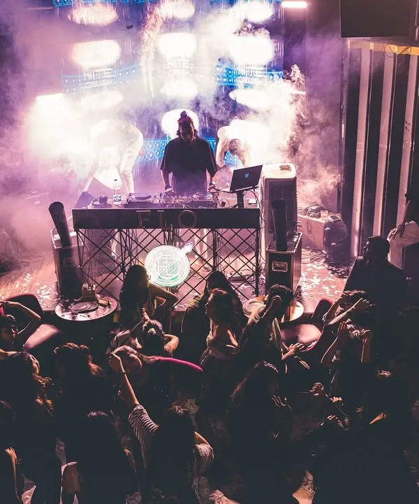 From my perspective behind the console, commanding a packed dance floor under a haze of purple lights and smoke. This is a typical high-energy night where the music takes over.