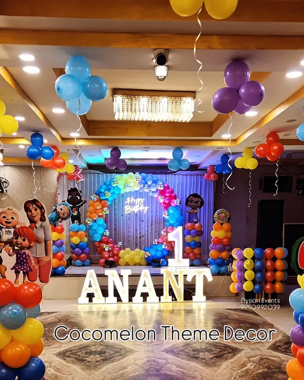 A vibrant Cocomelon theme for Anant's first birthday, filling the entire stage. This setup includes character cutouts, themed balloon columns, a rainbow balloon arch, and large LED letters spelling out the name.