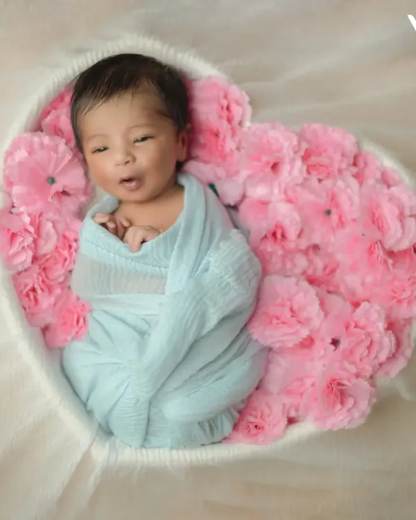 Even when they're awake, we can capture beautiful moments. This little one is nestled safely in a heart-shaped floral basket, a popular setup for our artistic newborn photography.