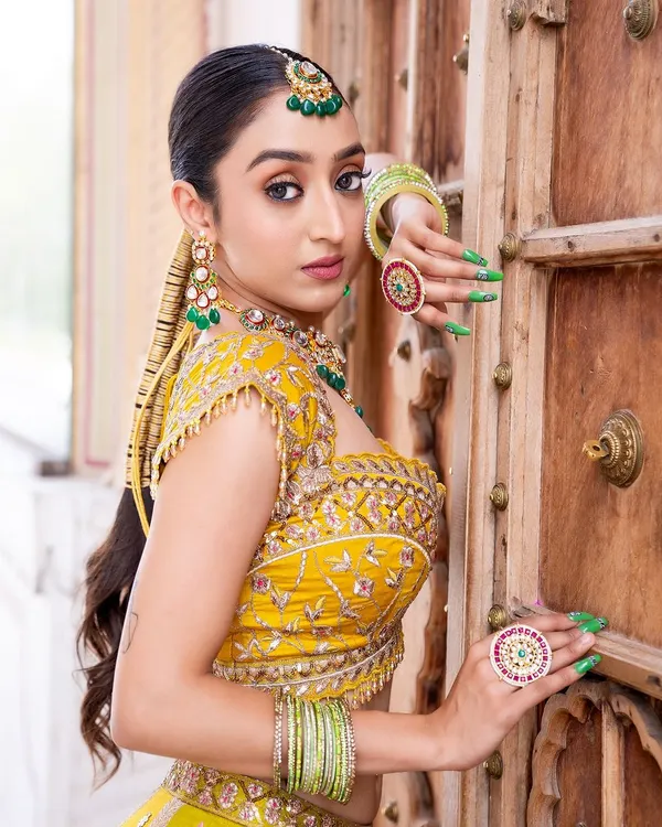 For a Mehendi function, a green-beaded jewellery set is a perfect choice. This model wears a Kundan choker with matching earrings, maang tikka, and statement rings that complement her yellow outfit beautifully.