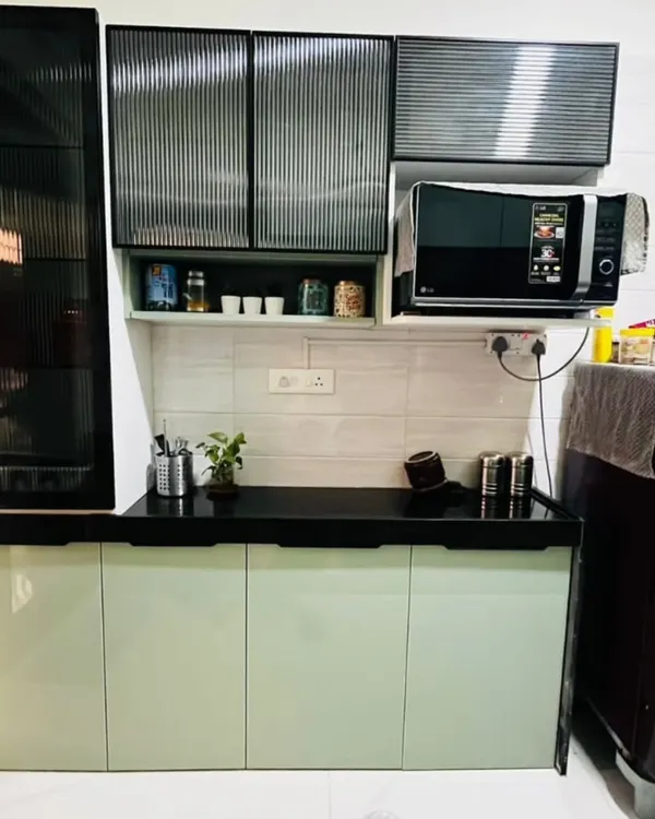 A modern kitchen design featuring serene sage green base cabinets and upper cabinets with trendy fluted glass. The black countertop and dedicated microwave unit complete the contemporary look.