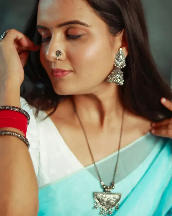 A beautifully detailed shot focusing on a pair of traditional silver jhumkas and a matching necklace. The shallow depth of field draws the eye directly to the jewelry.