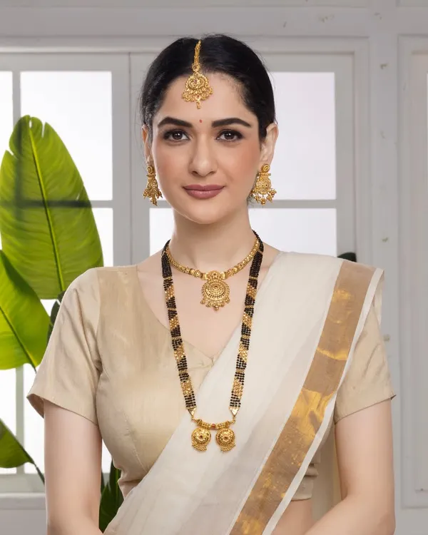 A classic portrait of a model wearing a traditional Mangalsutra and matching gold jewelry, set against a clean background to keep the focus entirely on the product's elegance.