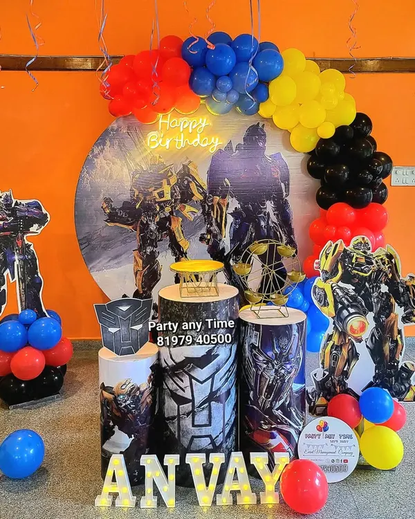 An action-packed Transformers theme for Anvay's birthday. This setup features large character cutouts, a themed backdrop, matching plinths, and a balloon arch in the classic red, blue, yellow, and black colors.