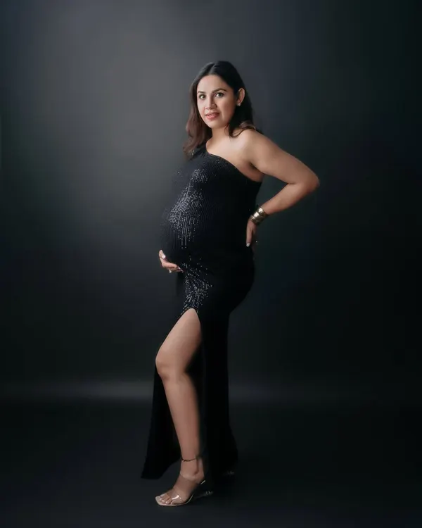 A full-length solo portrait of a mom-to-be looking powerful and elegant in a black one-shoulder sequin gown. This studio shot showcases a glamorous and confident maternity style.