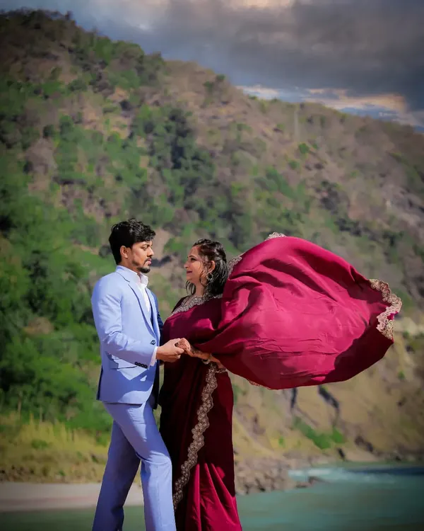 A cinematic shot of a couple against the backdrop of the Rishikesh mountains, with the bride's saree flowing in the wind.