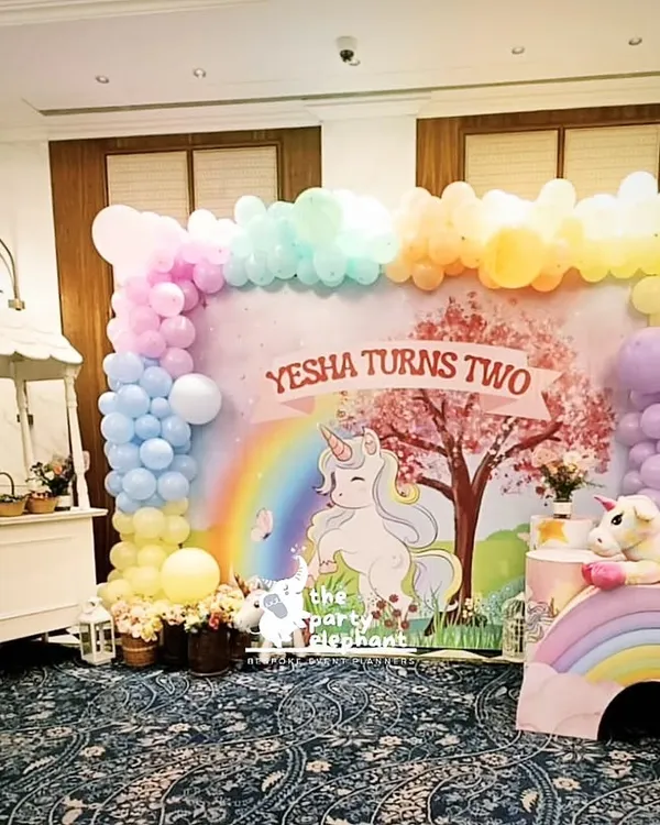 For Yesha's second birthday, I created a whimsical unicorn wonderland. This main backdrop features a custom illustration with a rainbow and unicorn, framed by a pastel balloon garland and complemented by a charming candy cart for treats.