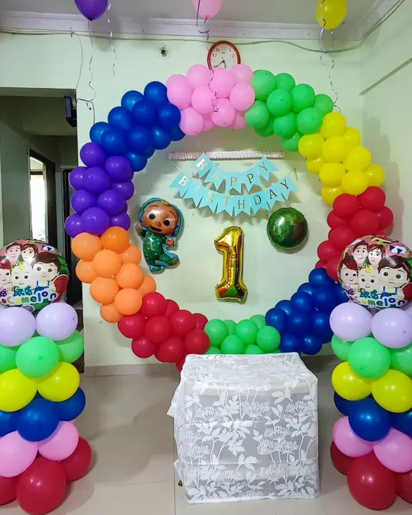 A vibrant Cocomelon theme for a first birthday, featuring a full ring balloon arch in all the colors of the rainbow. A Cocomelon character foil balloon and matching balloon columns complete this cheerful setup, perfect for a toddler's party.