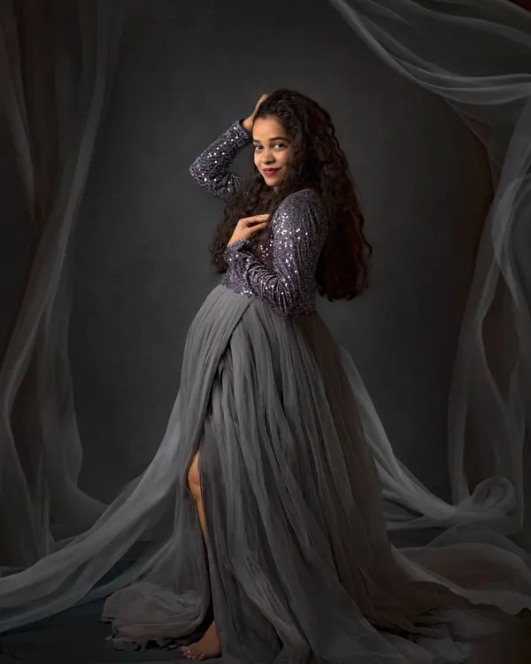 Creating a dreamy, ethereal look with flowing fabrics. This maternity session combines a glamorous sequined gown with soft, sheer drapes for a truly magical portrait against a classic studio backdrop.