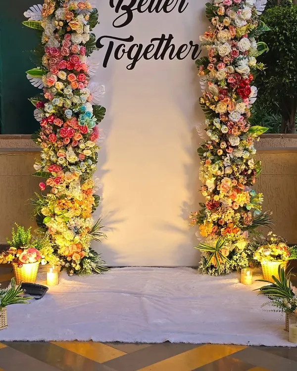 A close-up of the dense floral pillars used for the "Better Together" backdrop. The arrangement includes a variety of roses and other flowers in shades of pink, yellow, and white.