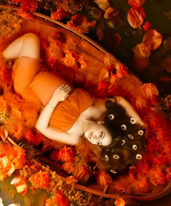 A truly unique fine art maternity portrait. This overhead shot captures an expectant mother peacefully resting in a boat, surrounded by a sea of orange petals and fabric, creating a breathtaking and artistic scene.